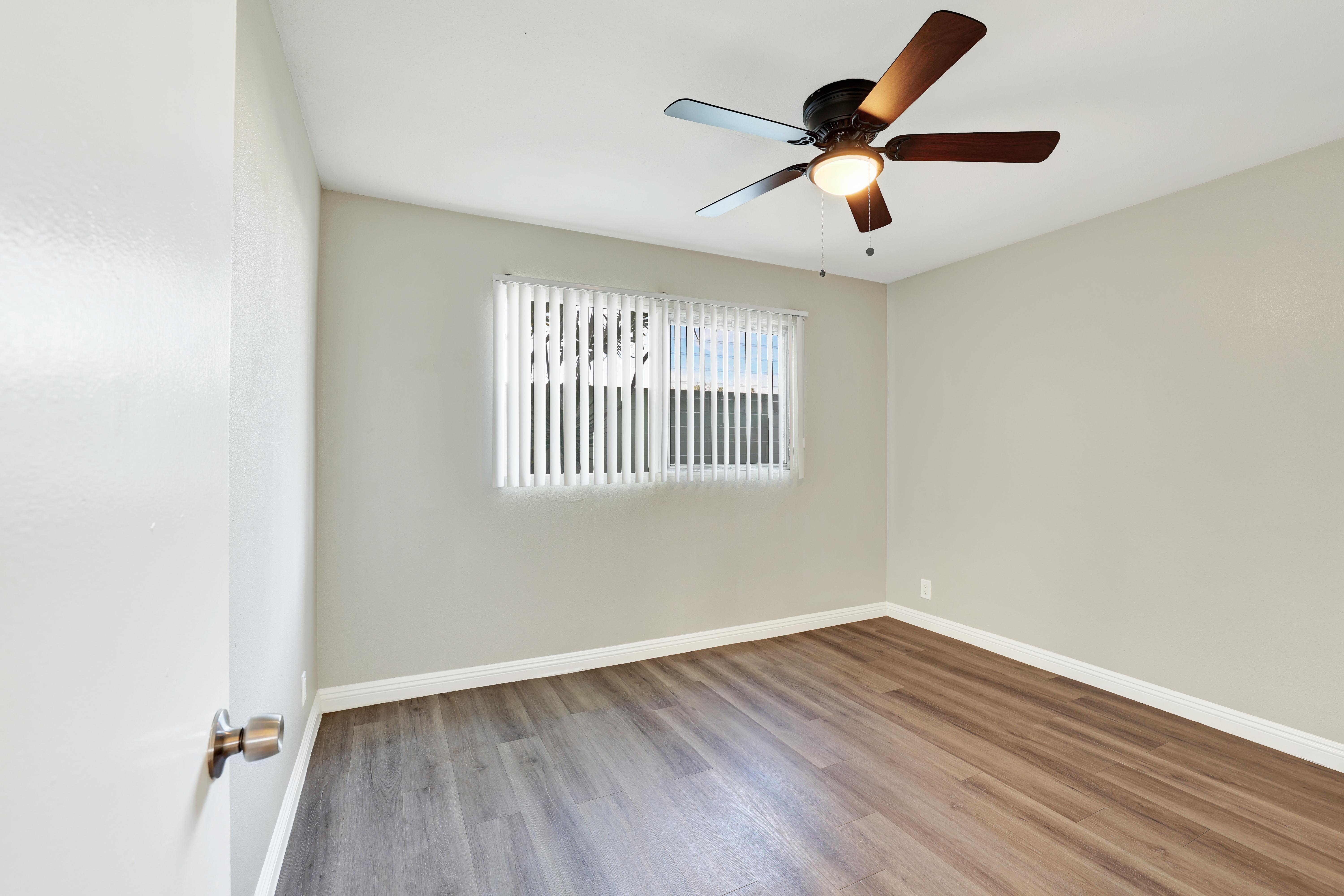 A room with a ceiling fan and a window with blinds.