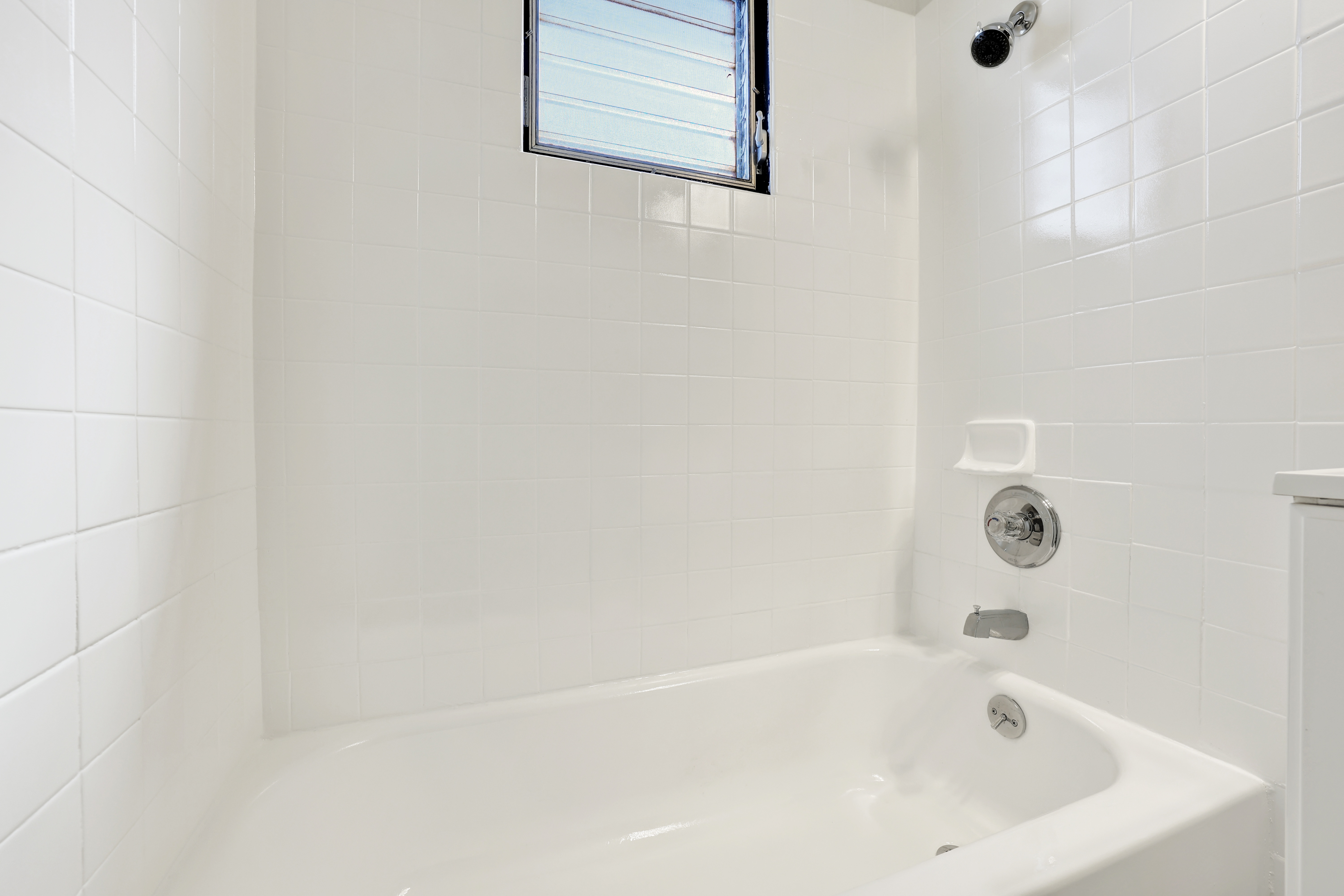 A white bathtub with a shower head and a window above it.