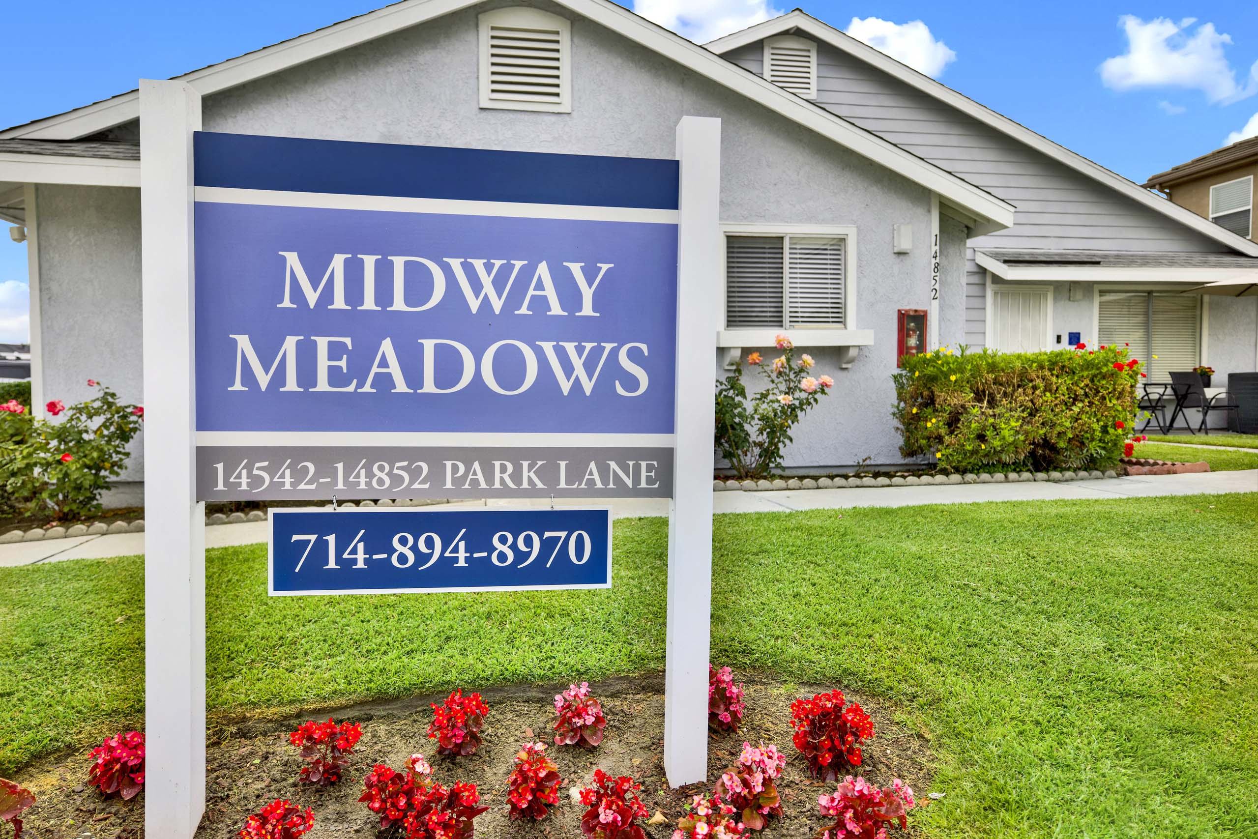 A sign for Midway Meadows with a house in the background.