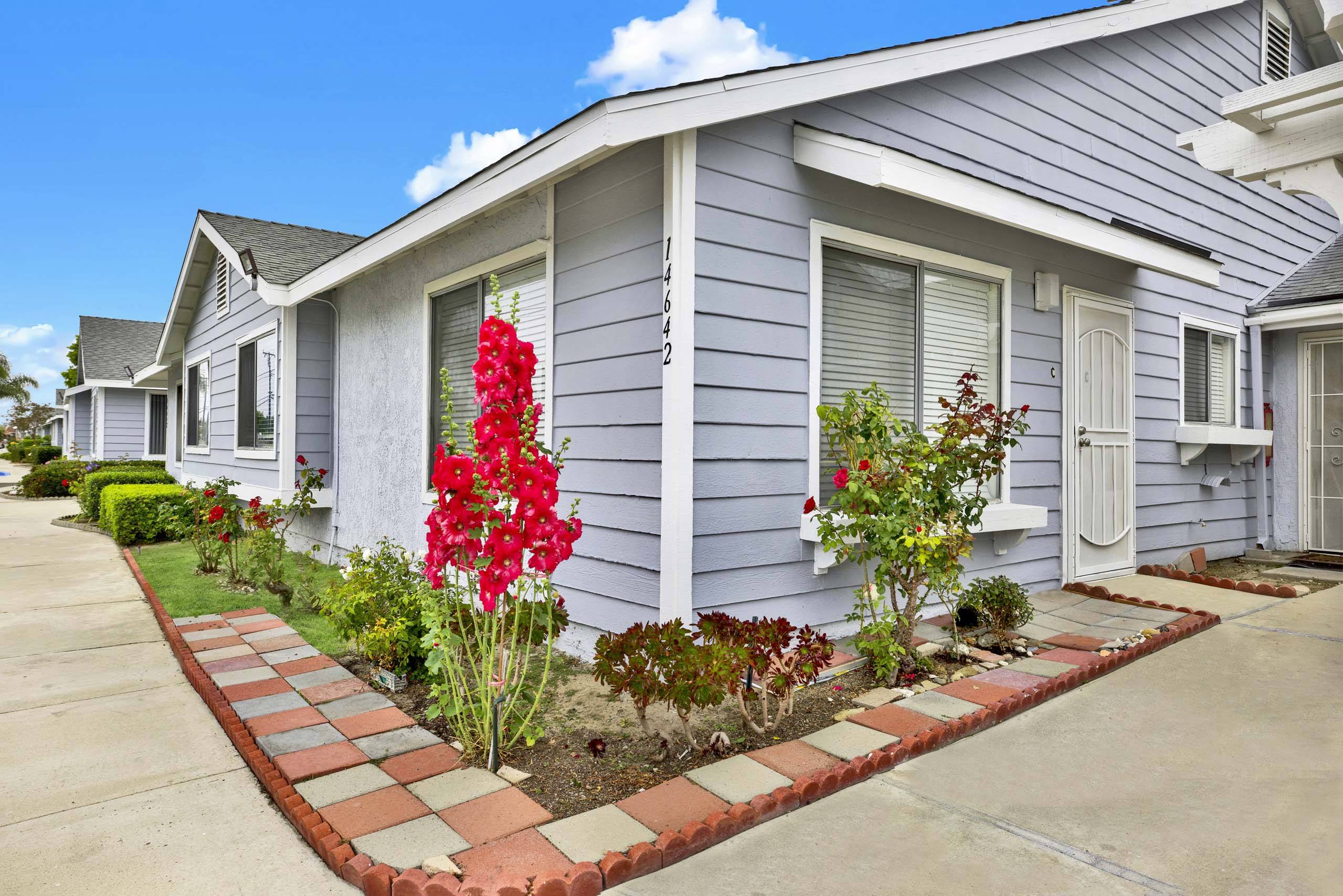 A house with a grey siding and a red flower in front.