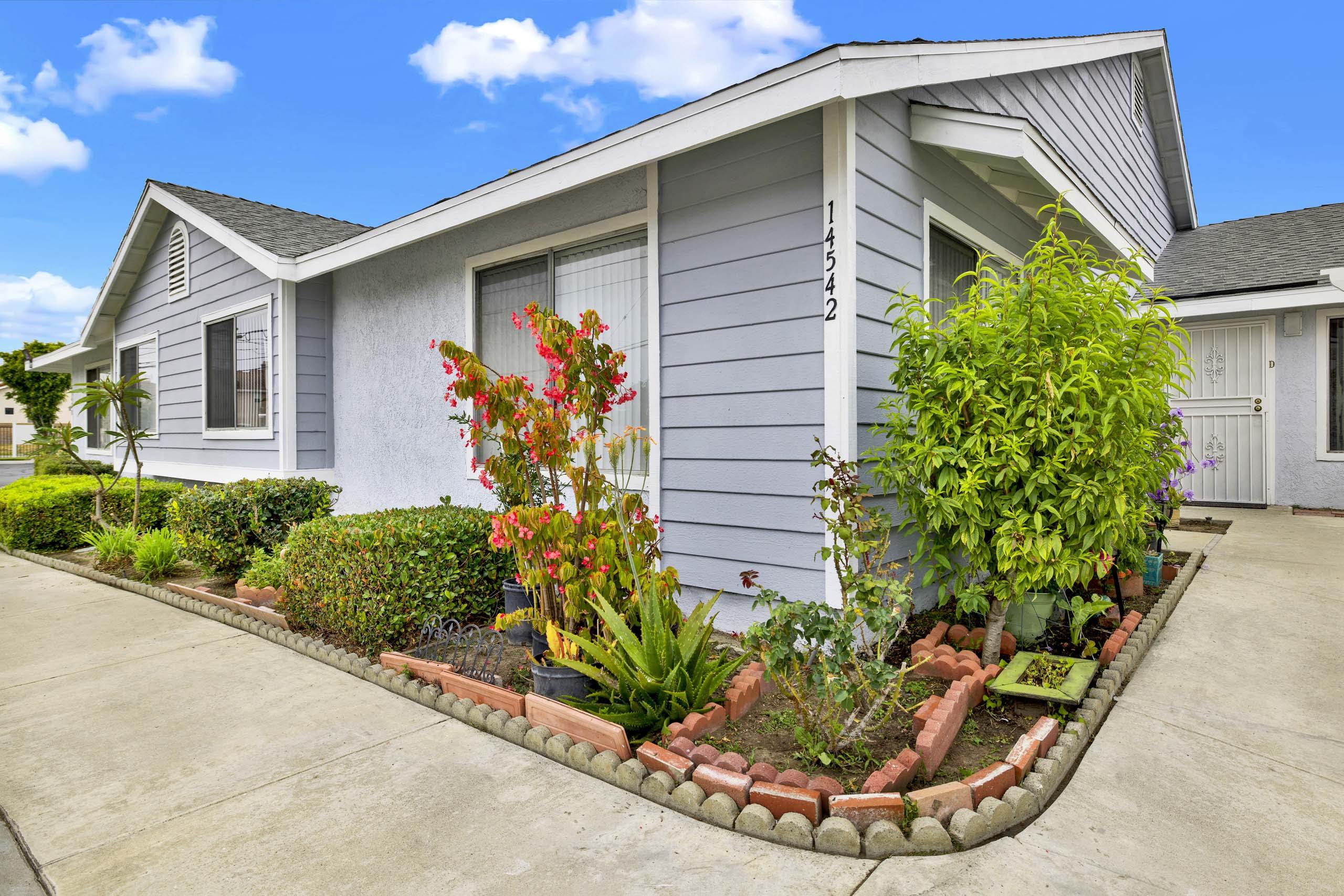 A house with a grey siding and a red brick flower bed in front.