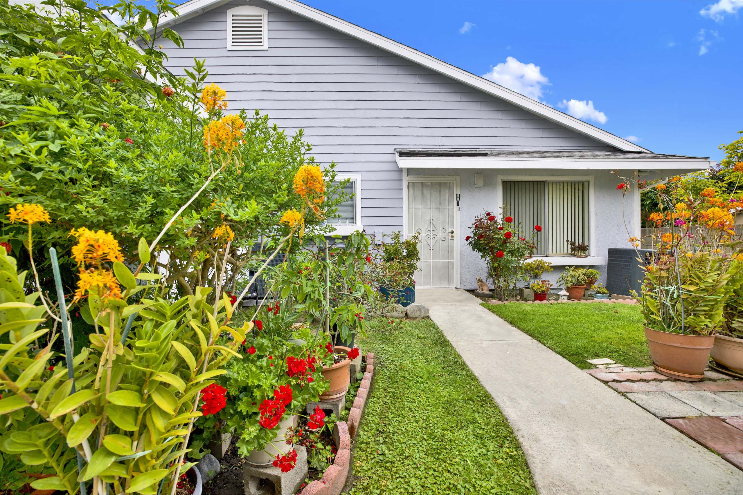 A house with a grey roof and white walls is surrounded by a garden with red and yellow flowers.