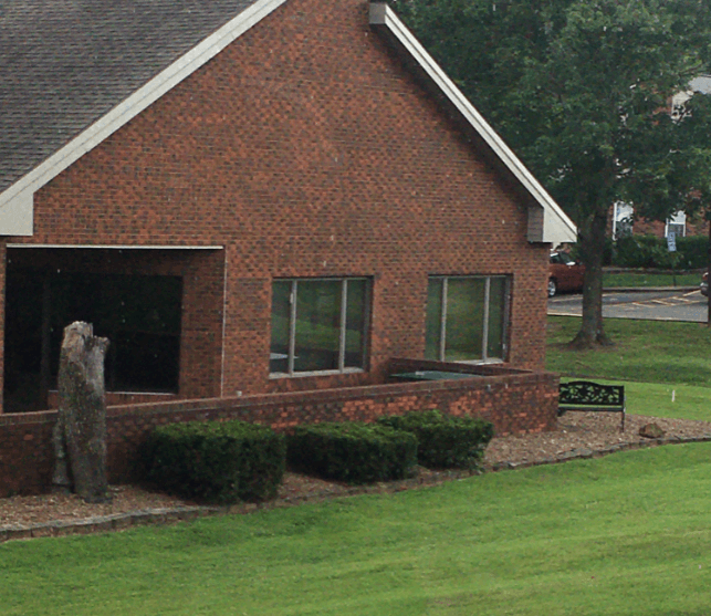 the side of a brick building with a lawn and hedges