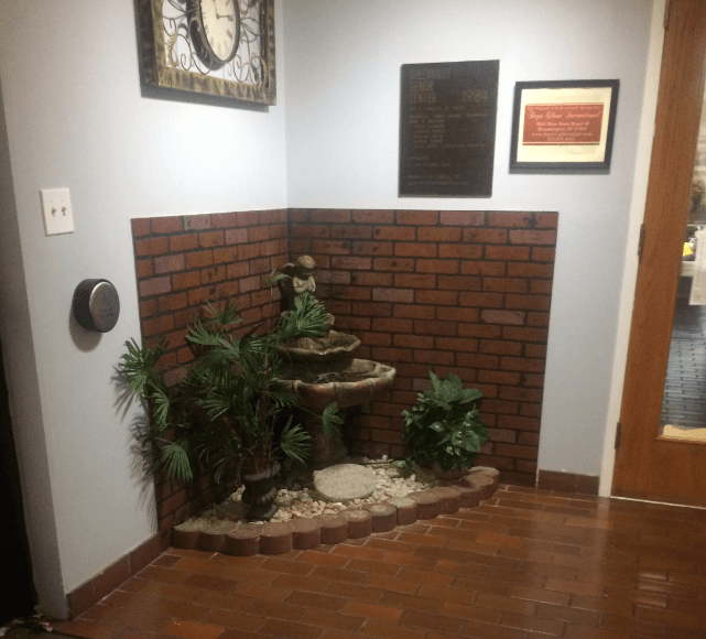 a small fountain in the corner of a brick wall with plants