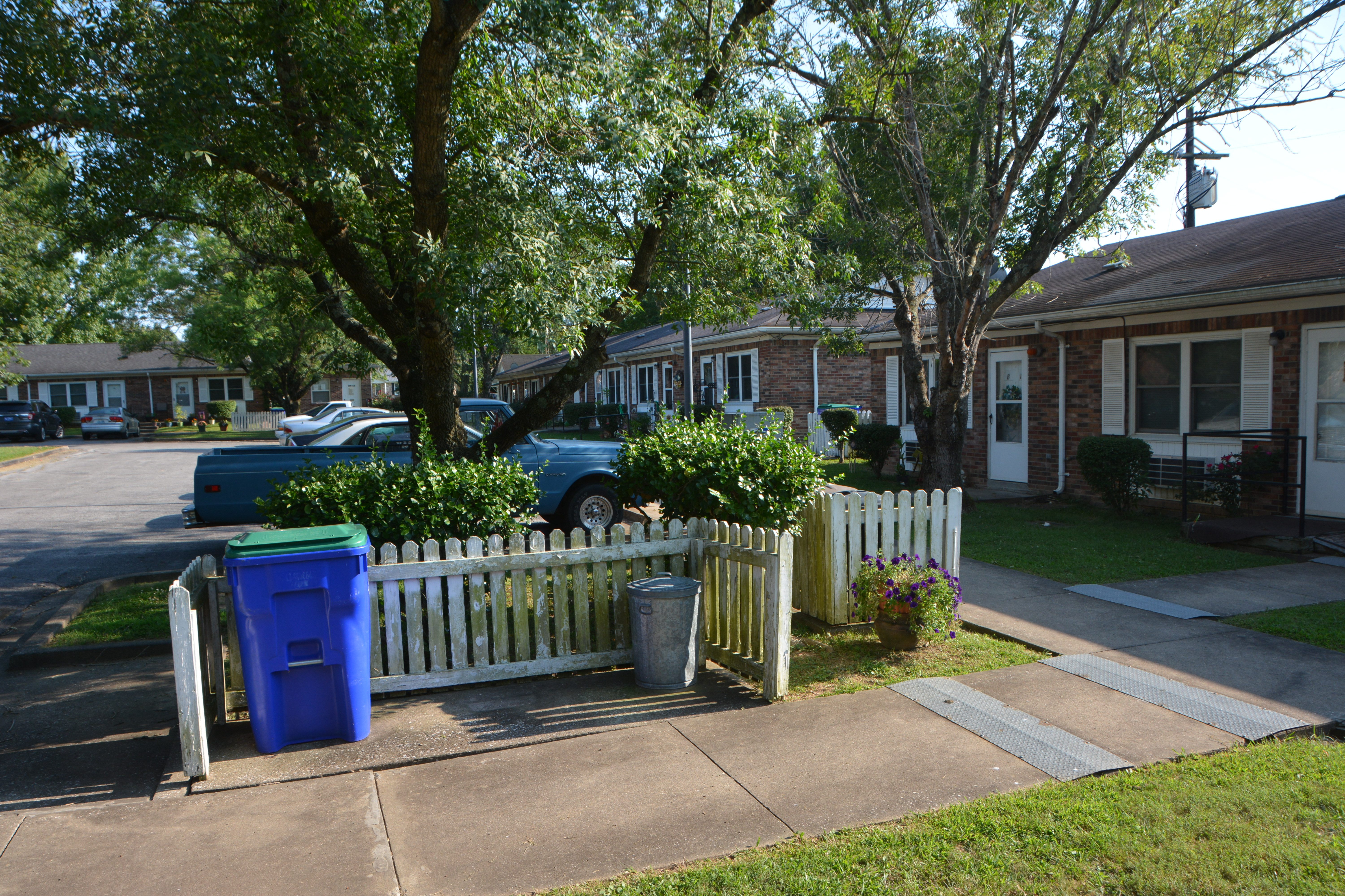 a white fence in front of a house with a blue trash can