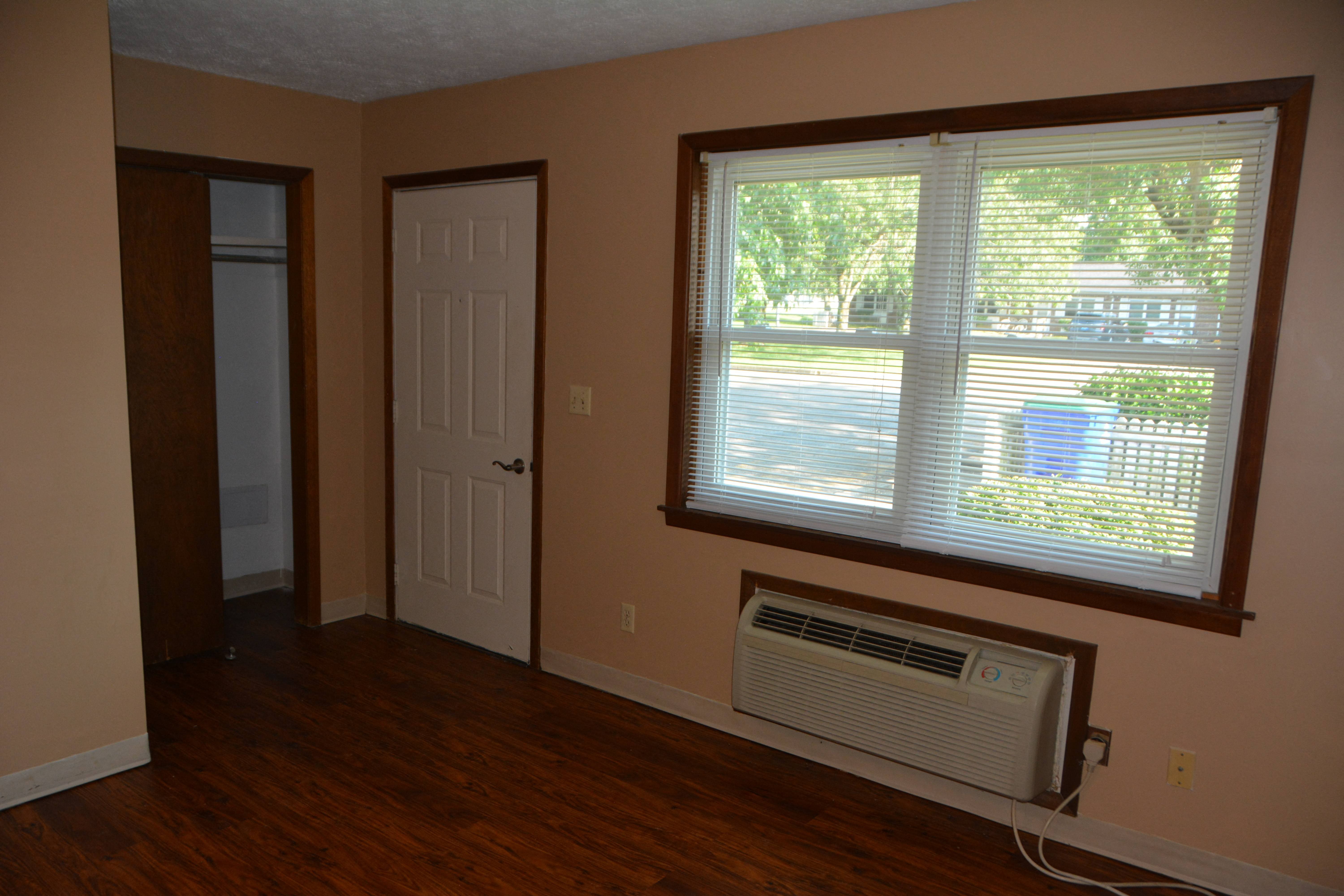 an empty living room with a window and a air conditioner