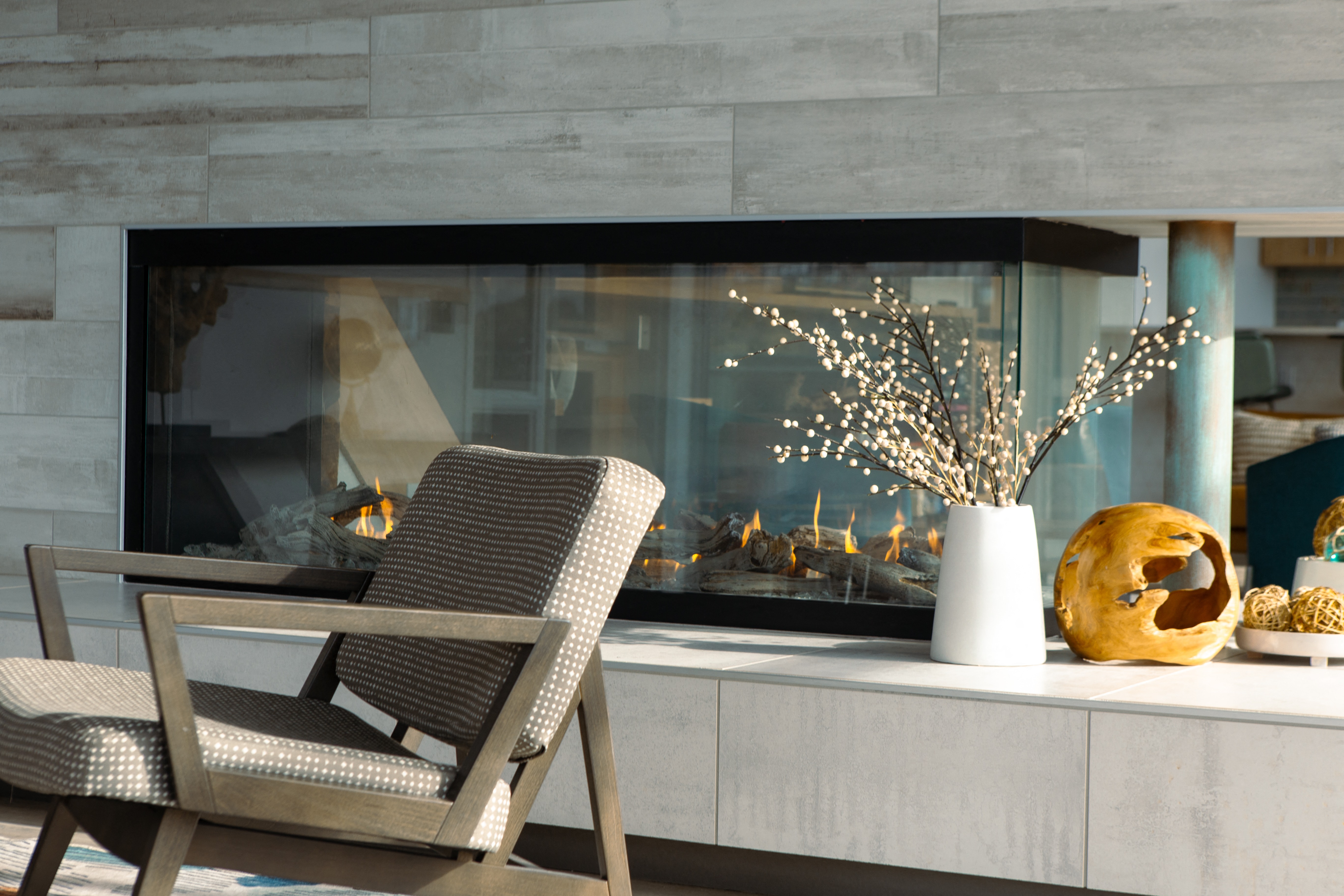 a fireplace in a living room with two chairs and a vase of flowers