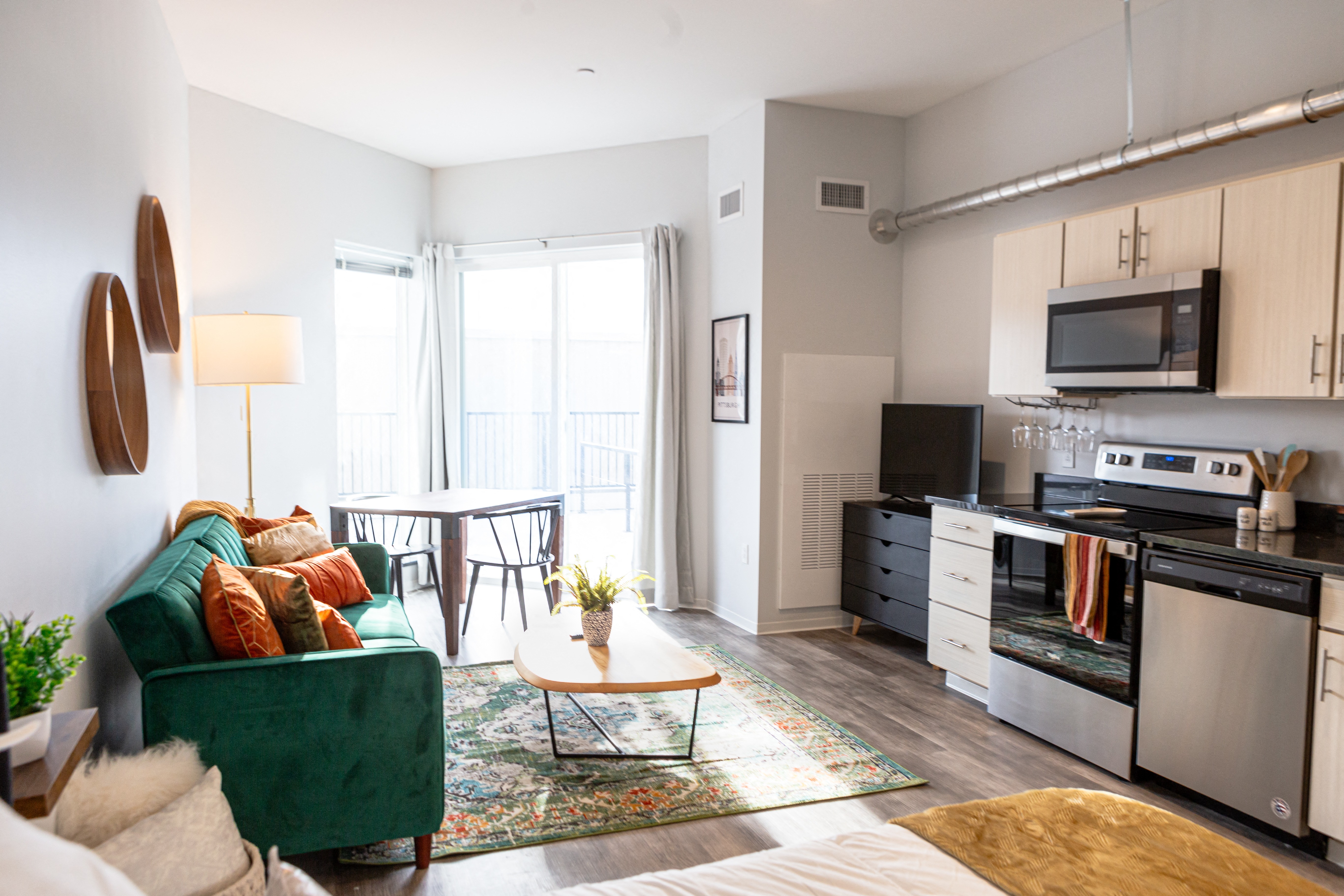 a living room with a green couch and a kitchen with a stove and a microwave