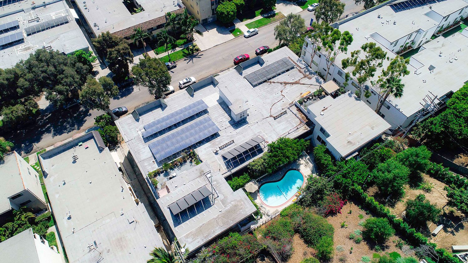 Aerial drone view of Rose North Apartments showing solar panels, energy efficient roof, and courtyard with pool.