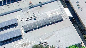 Aerial drone view of Rose North Apartments showing solar panels, energy efficient roof, and courtyard with pool.