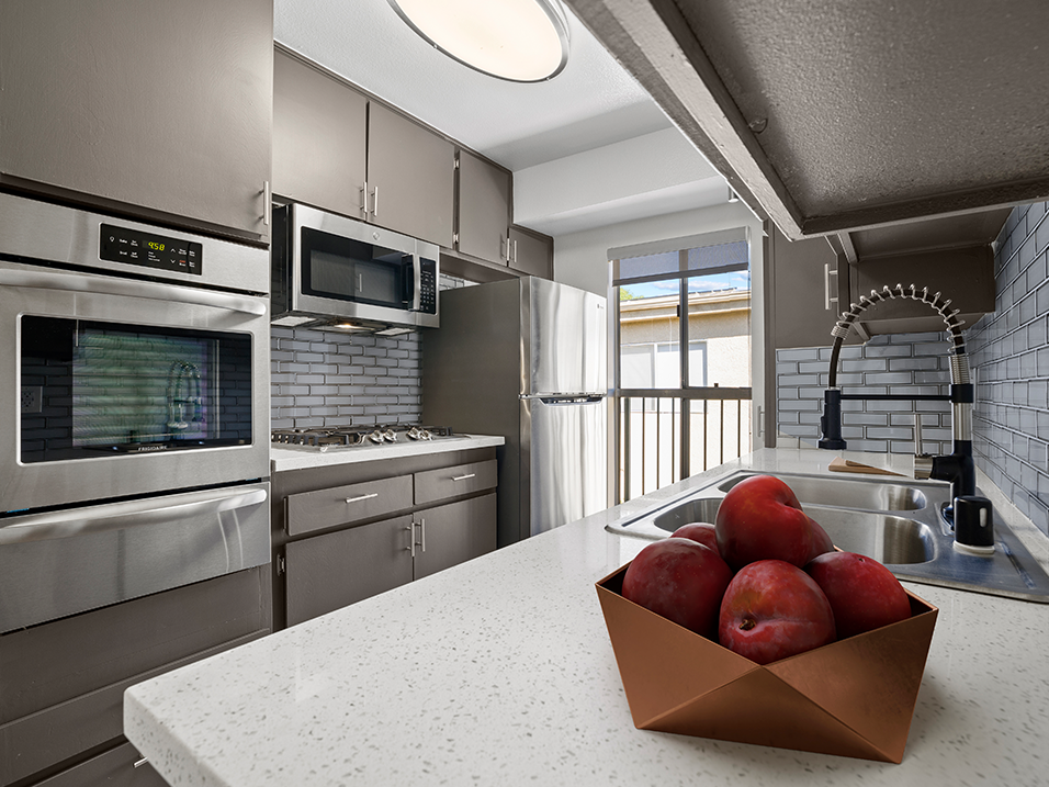 Blue tiled kitchen with stainless steel oven, microwave, fridge, and fixtures.