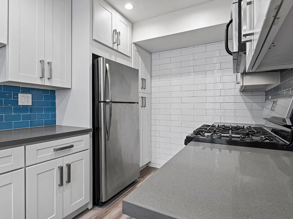 Blue tiled kitchen with stainless steel oven, fridge, and fixtures.