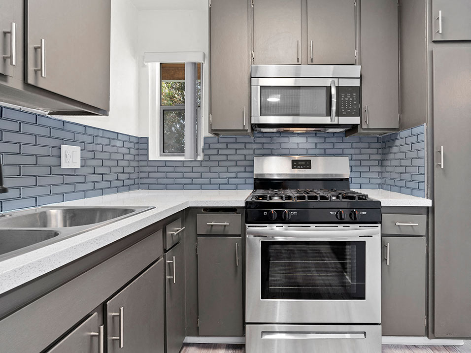 Blue tiled kitchen with stainless steel fridge, oven, and microwave.