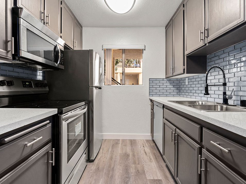 White tiled kitchen with stainless steel oven, microwave, and fridge..
