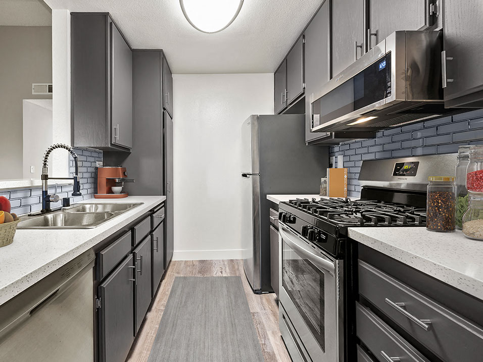 Blue tiled kitchen with stainless steel microwave, oven, and refrigerator.