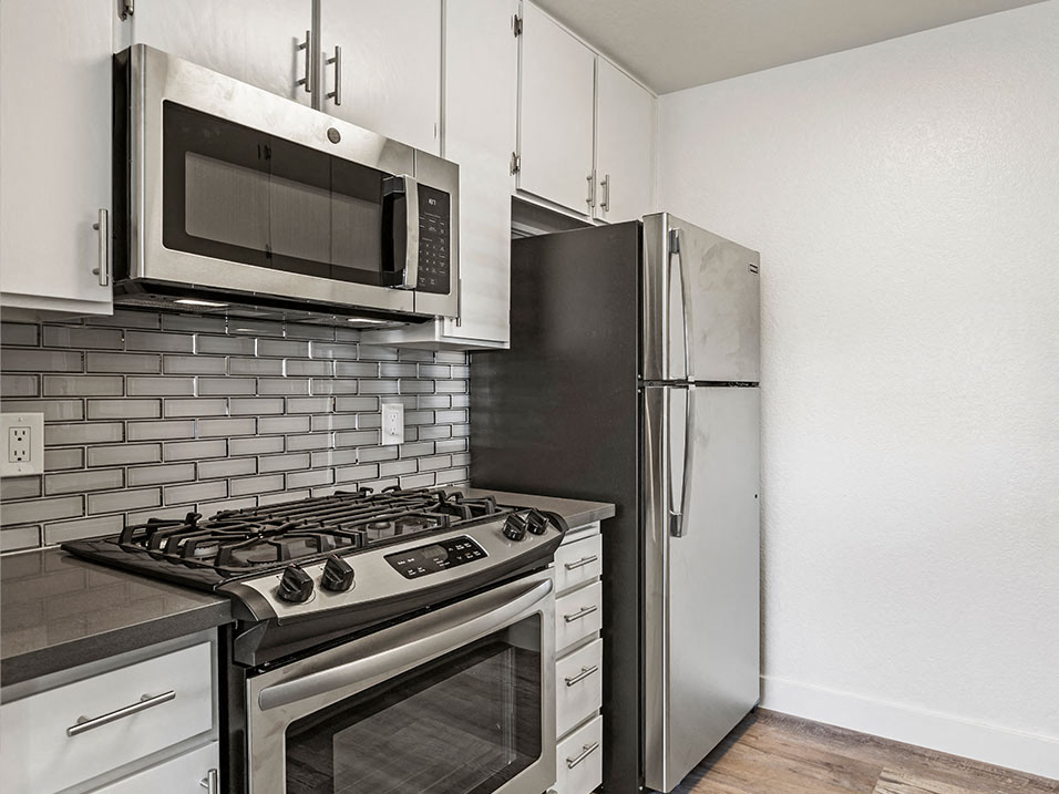 White tiled kitchen with stainless steel fridge, oven, and microwave.