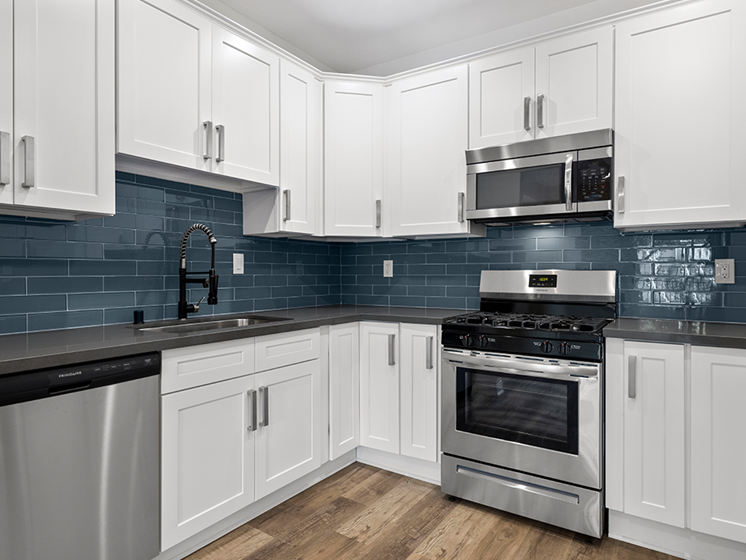 Blue tiled kitchen with stainless steel fridge, oven, and microwave.