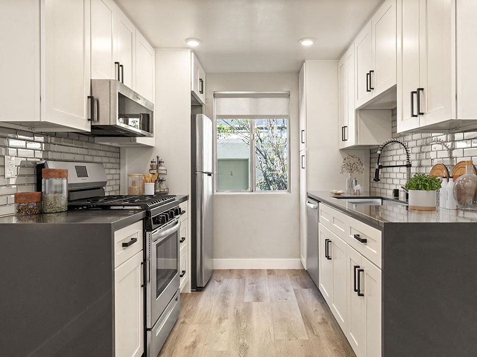 Tiled kitchen with stainless steel microwave, oven, fridge, and fixtures.