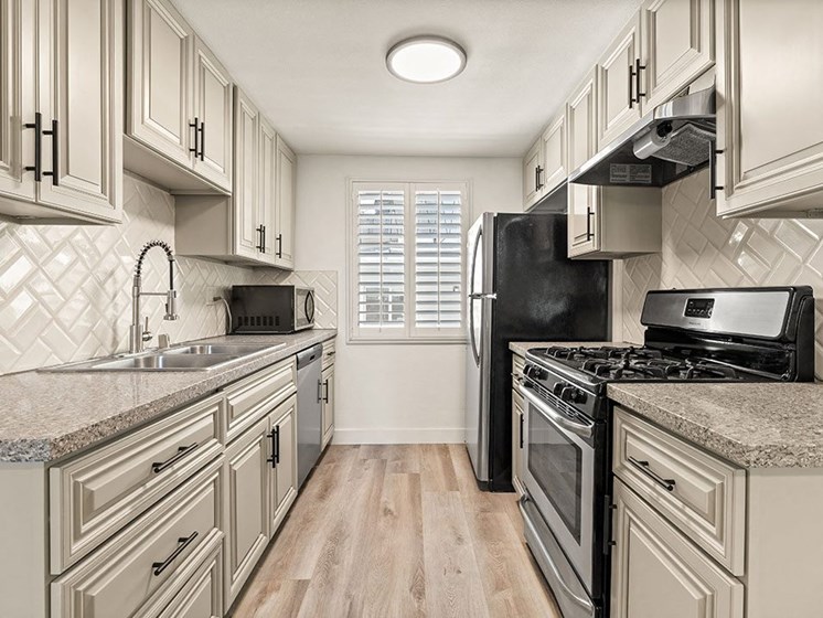 Tiled kitchen with stainless steel microwave, oven, fridge, and fixtures.