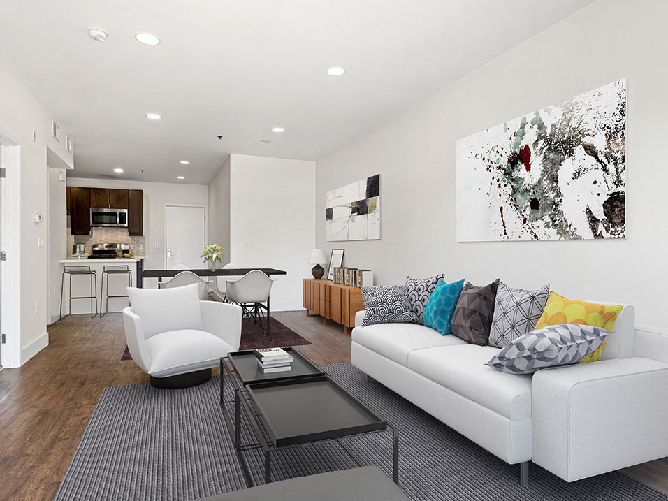 Hardwood floored living room with can lights and view of kitchen.