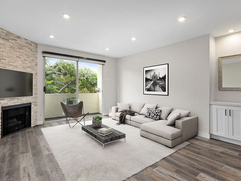 Hardwood floored living room with view of stone accent wall, fireplace, and private balcony.