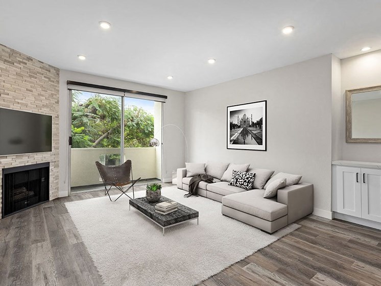 Hardwood floored living room with view of stone accent wall, fireplace, and private balcony.