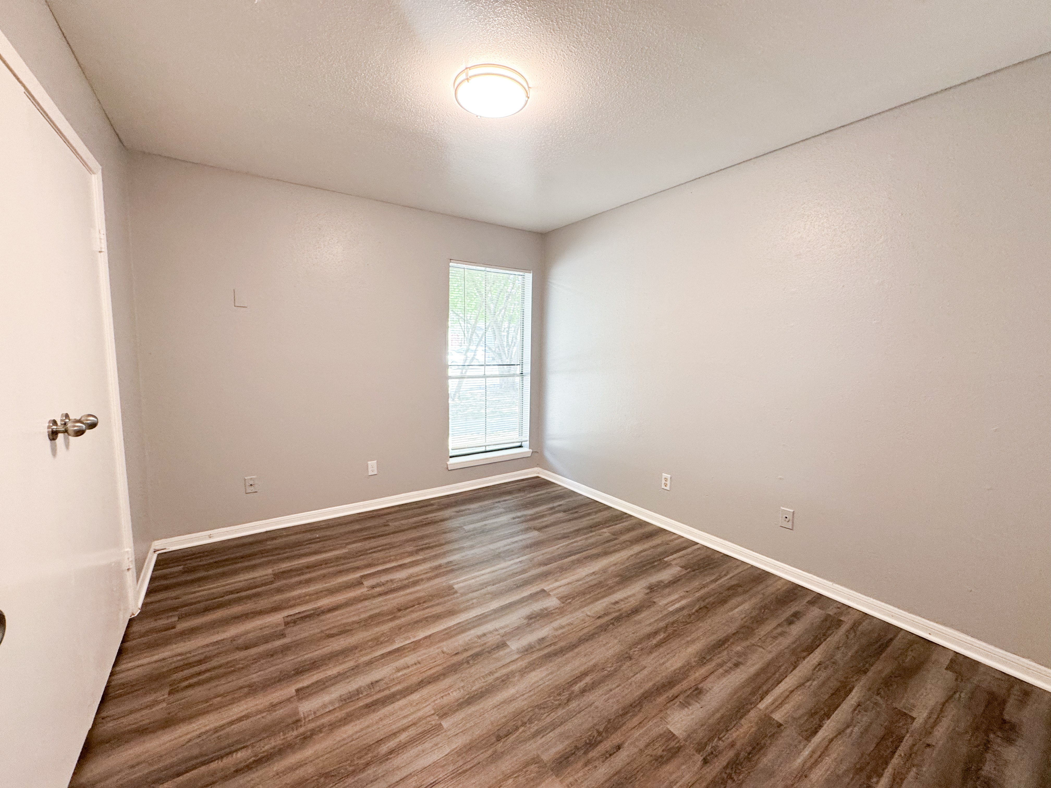 A room with wooden flooring and a door on the left.