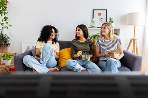 Three women are sitting on a couch, each holding a bowl of salad.