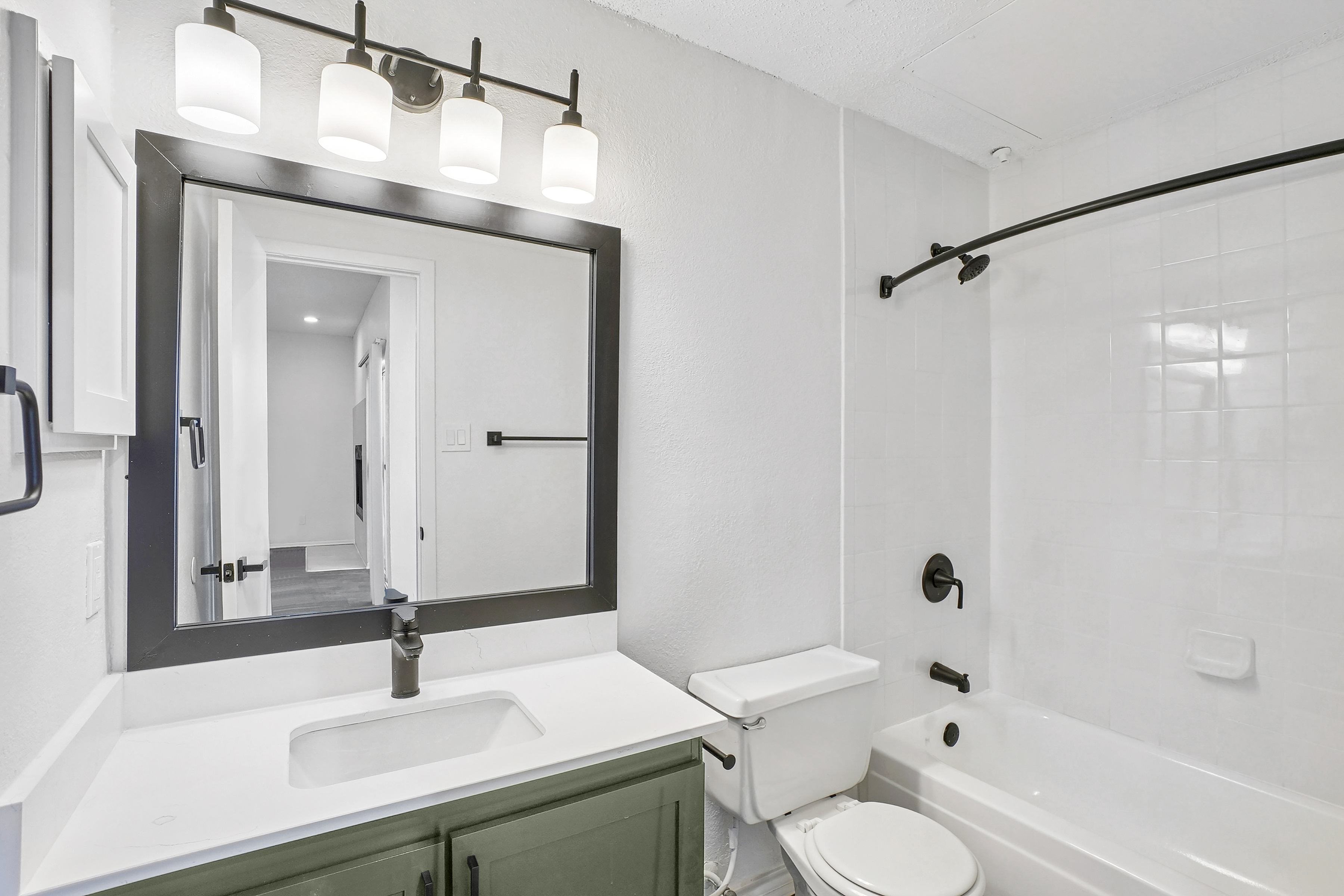 A white bathroom with a green cabinet and a black framed mirror.
