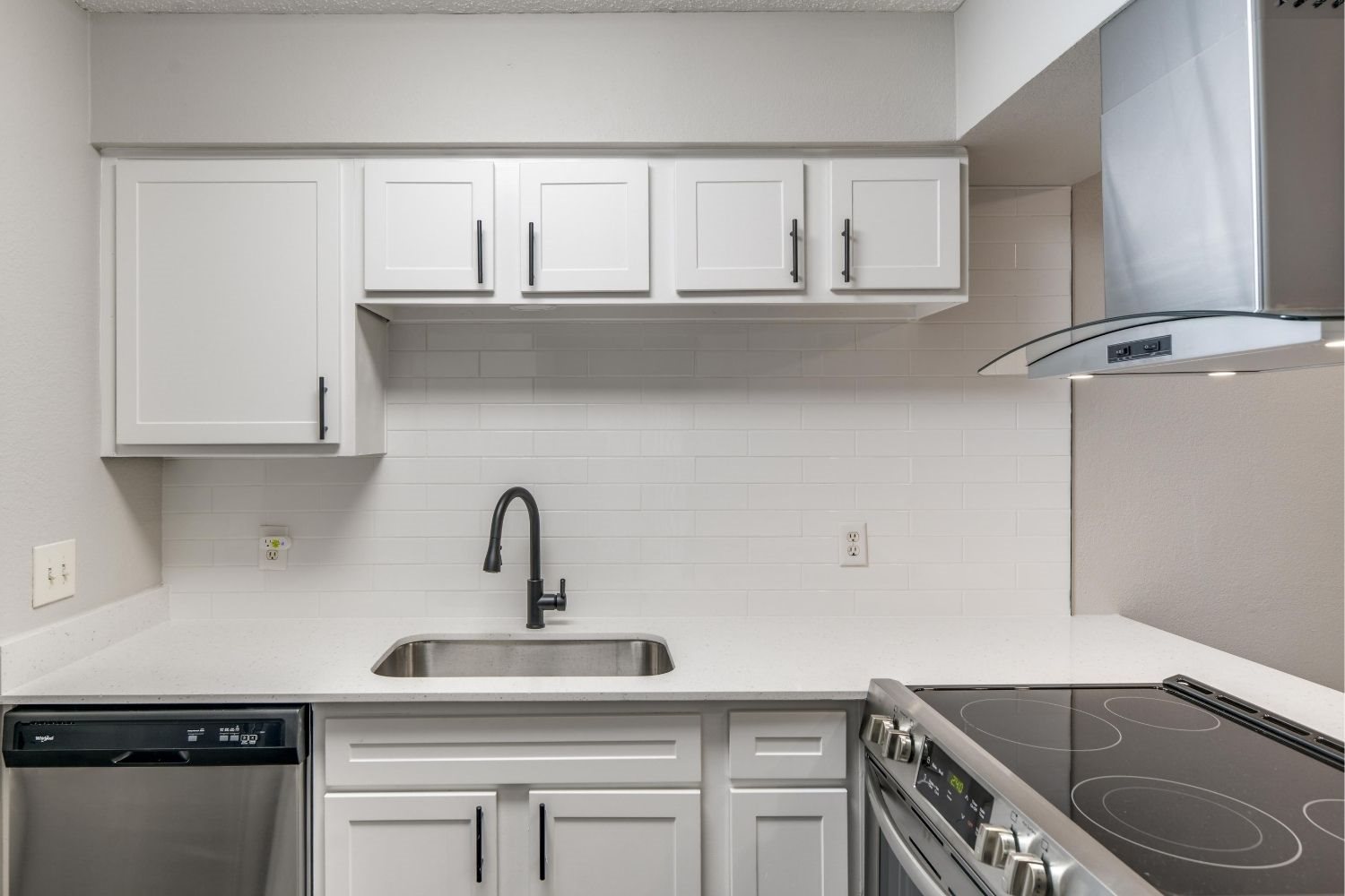 White kitchen counter with undermount sink, white tile backsplash, and electric range.