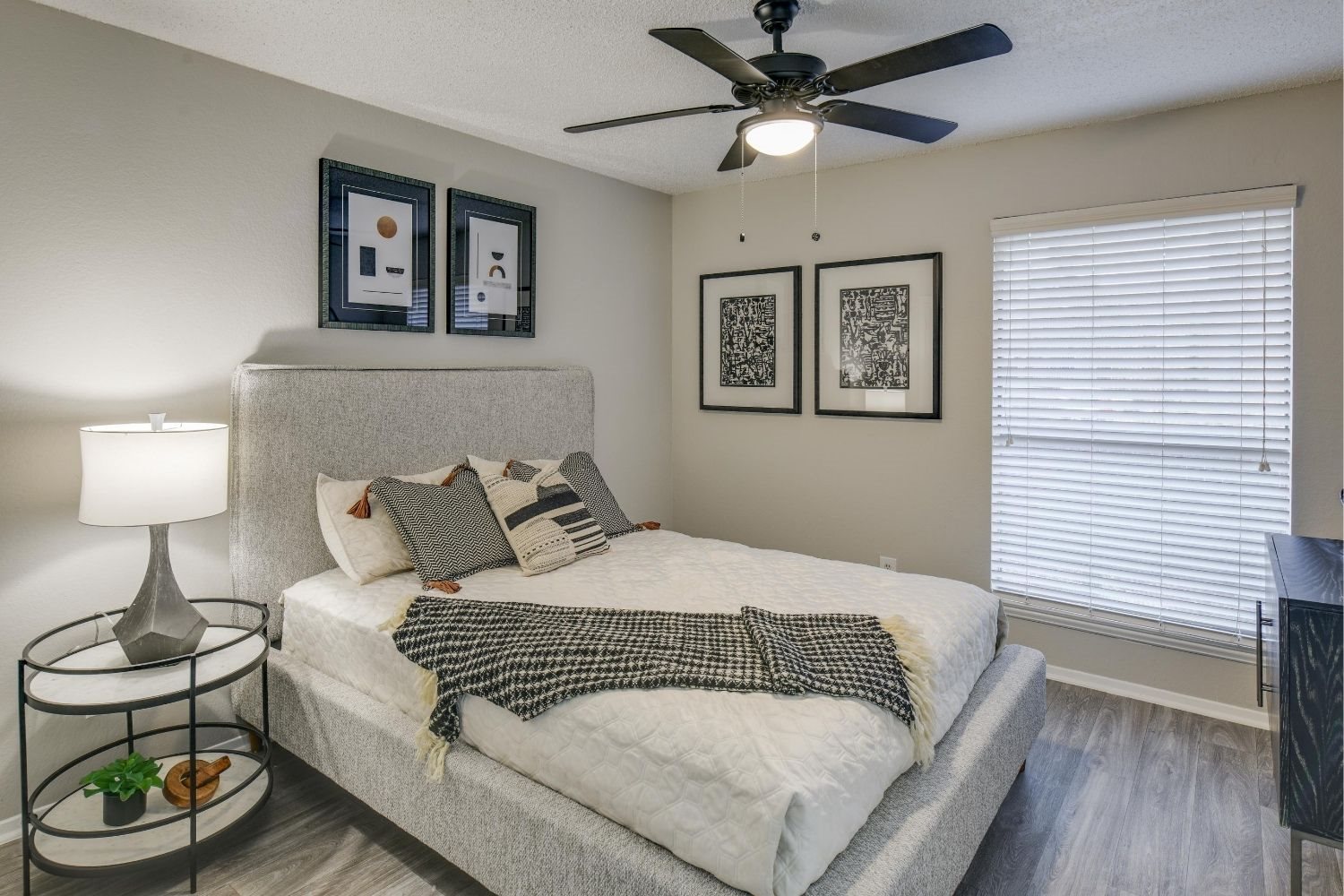 Serene bedroom with upholstered bed, ceiling fan, and large window blinds.