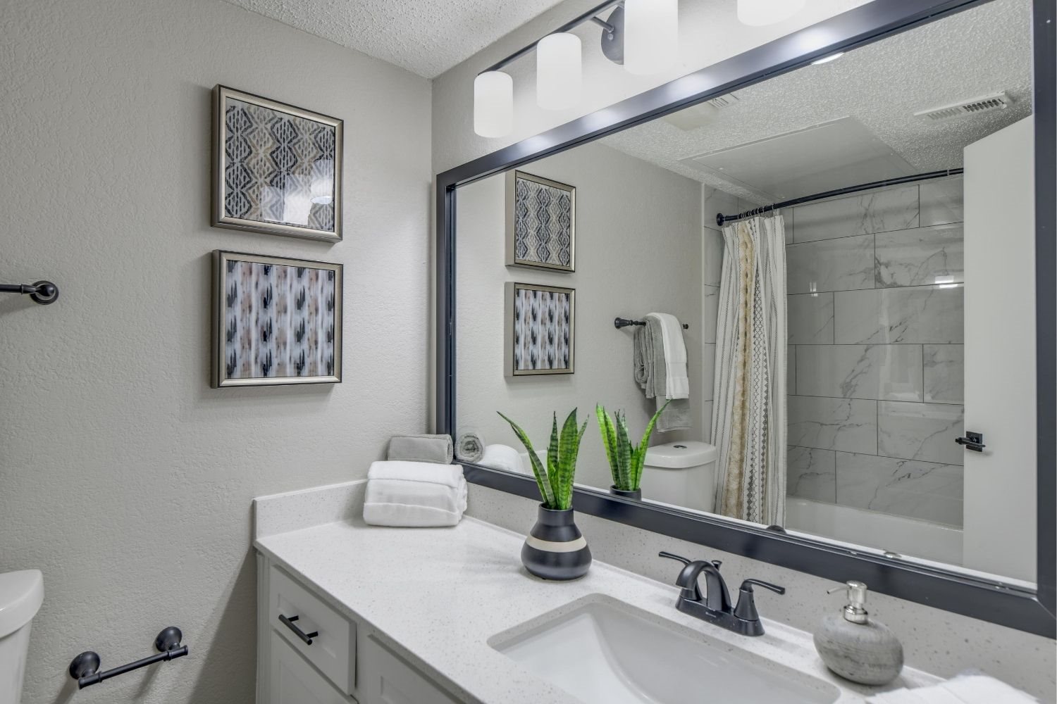 Updated bathroom vanity with oversized mirror, modern lighting, and black hardware.