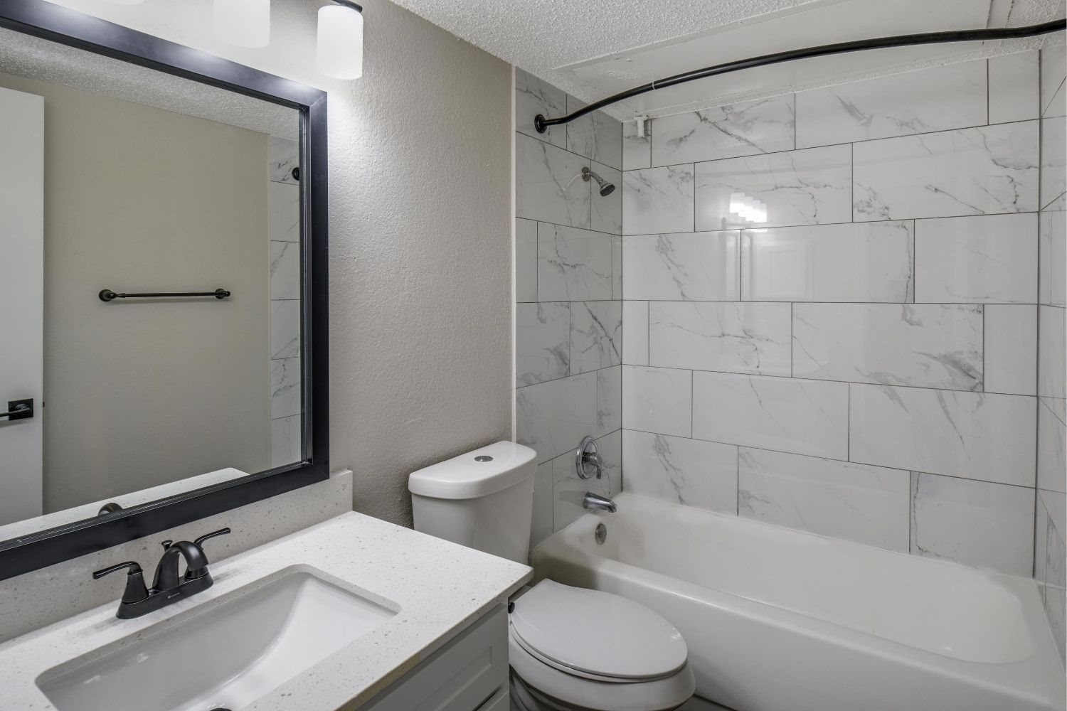 Bathroom with tub-and-shower combo, marble-look tile surround, and single-sink vanity.