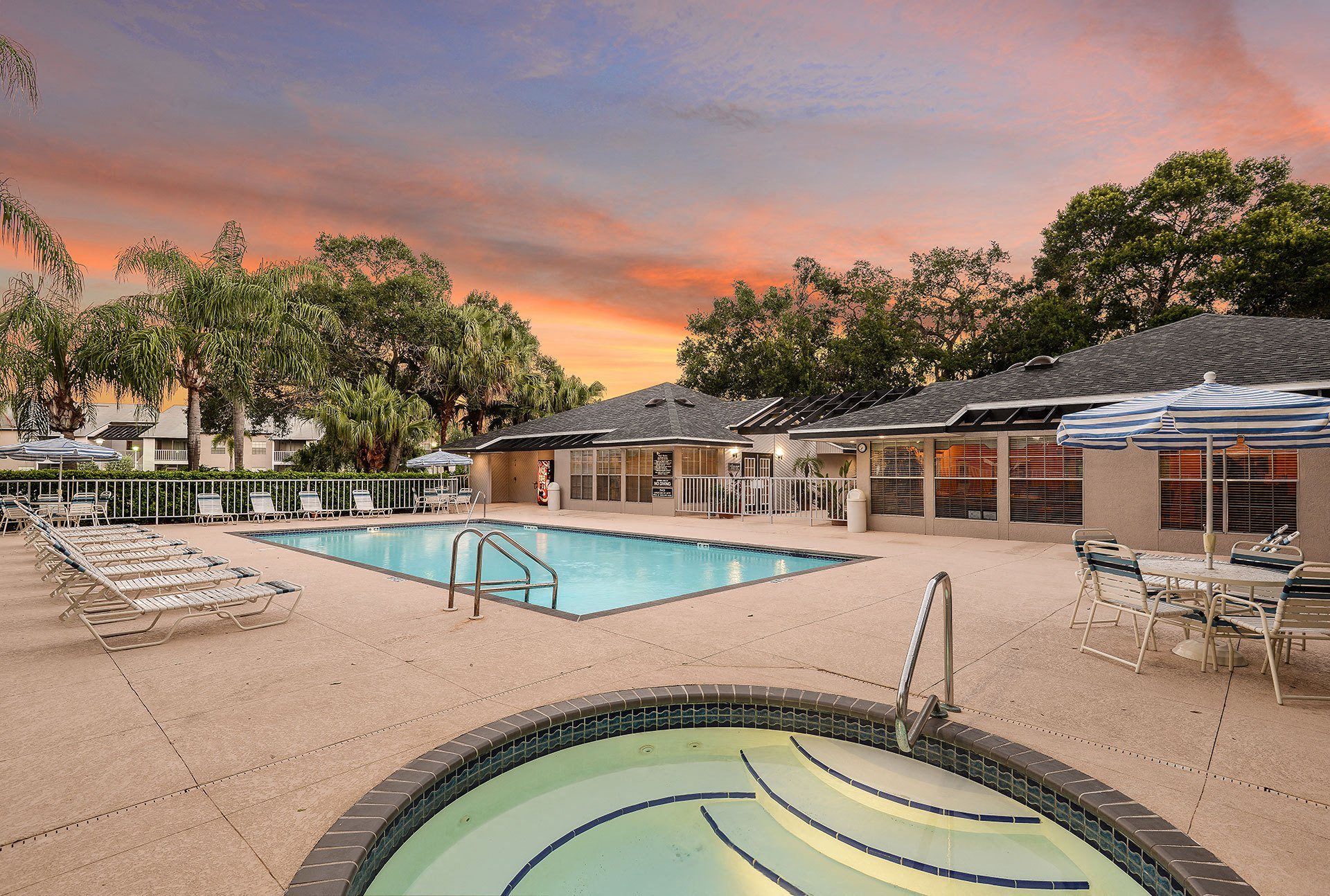 a swimming pool with chairs and umbrellas at sunset