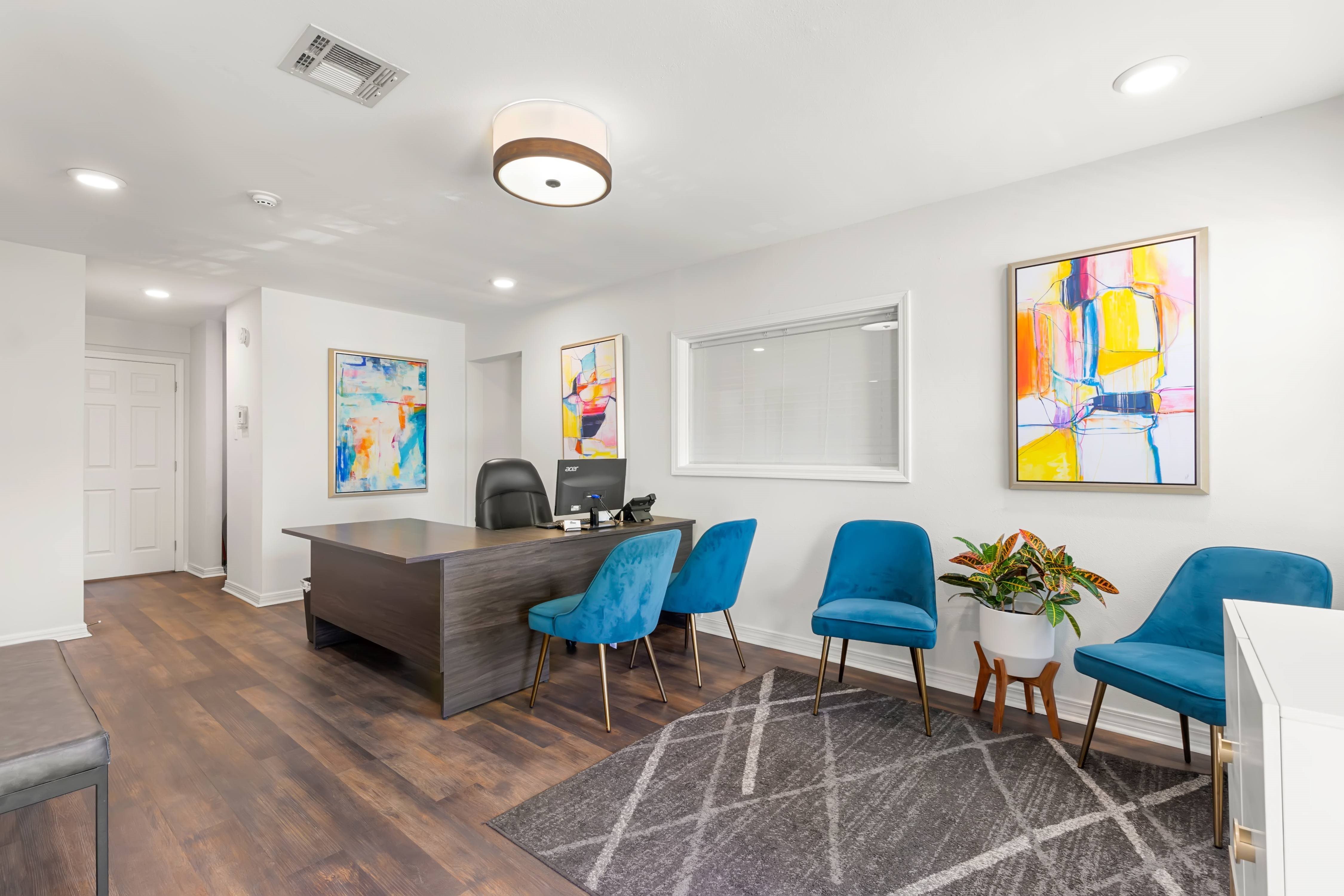 A room with a desk, chairs, and a painting on the wall.