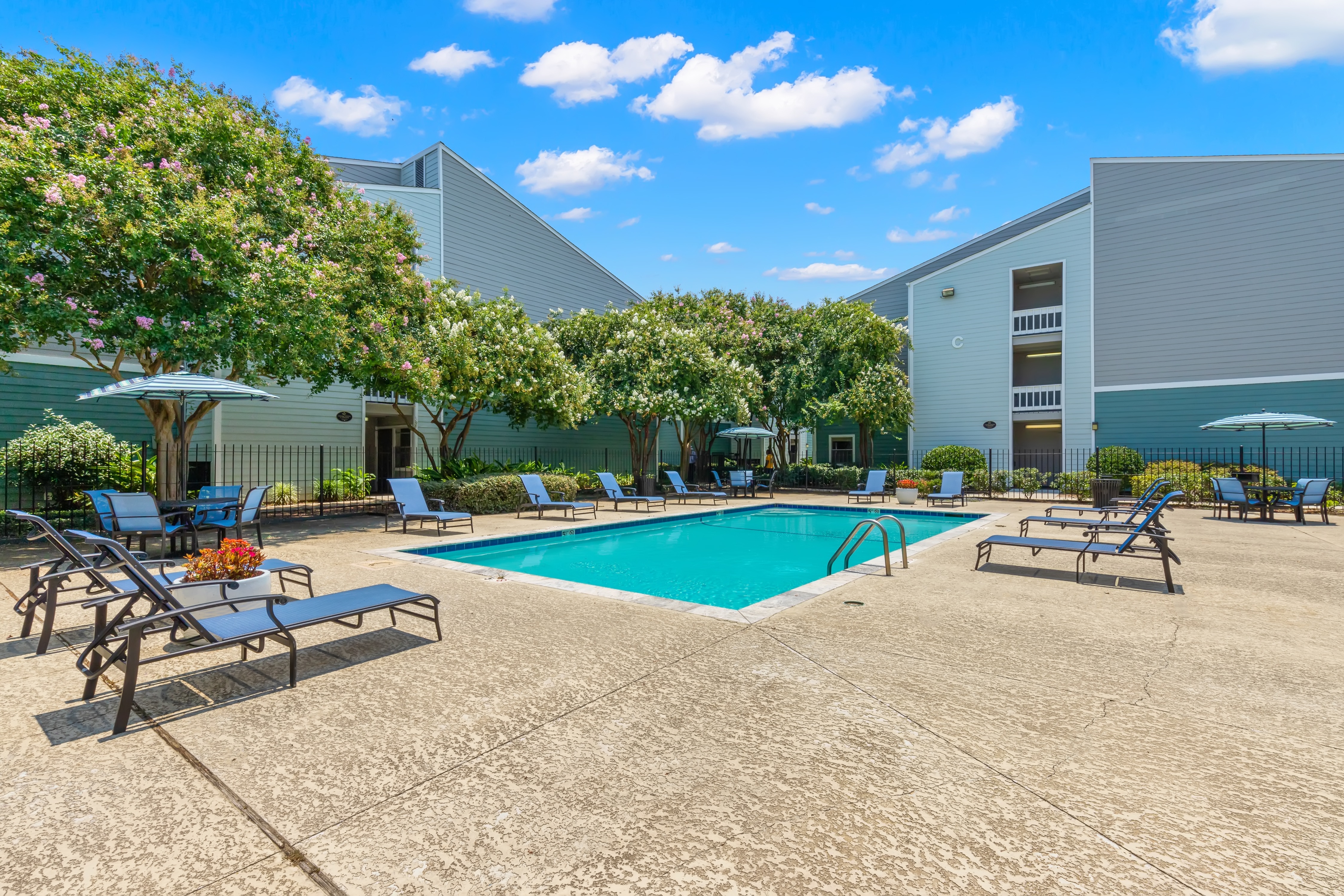 A pool surrounded by chairs and trees with a building in the background.