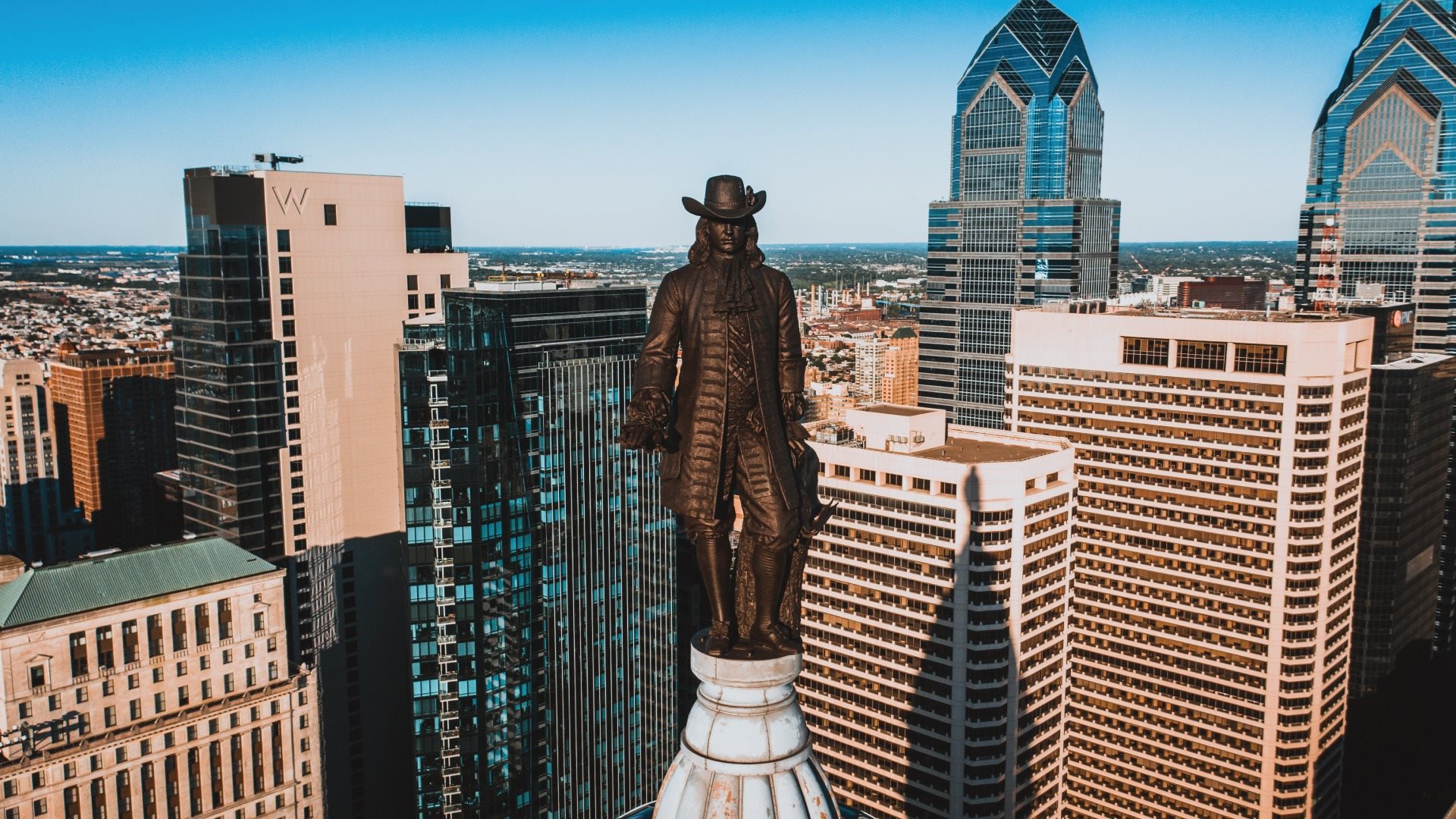 A statue of a man stands in front of a city skyline.