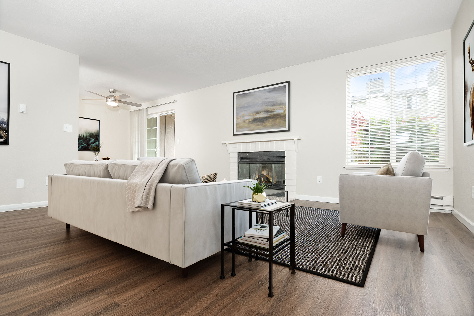 a living room with white walls, a fireplace, a couch, chairs and sunny windows at University Glen, University Place