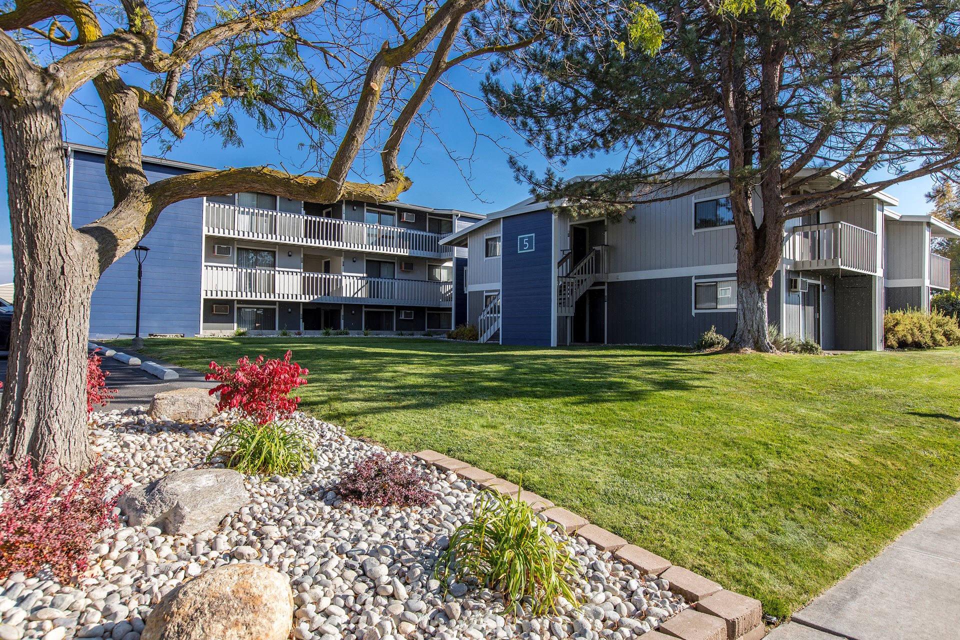 Outside sunny community with large grass lawn, trees, well-maintained landscaping and apartments behind.at The Lakes Apartments, Washington, 98837
