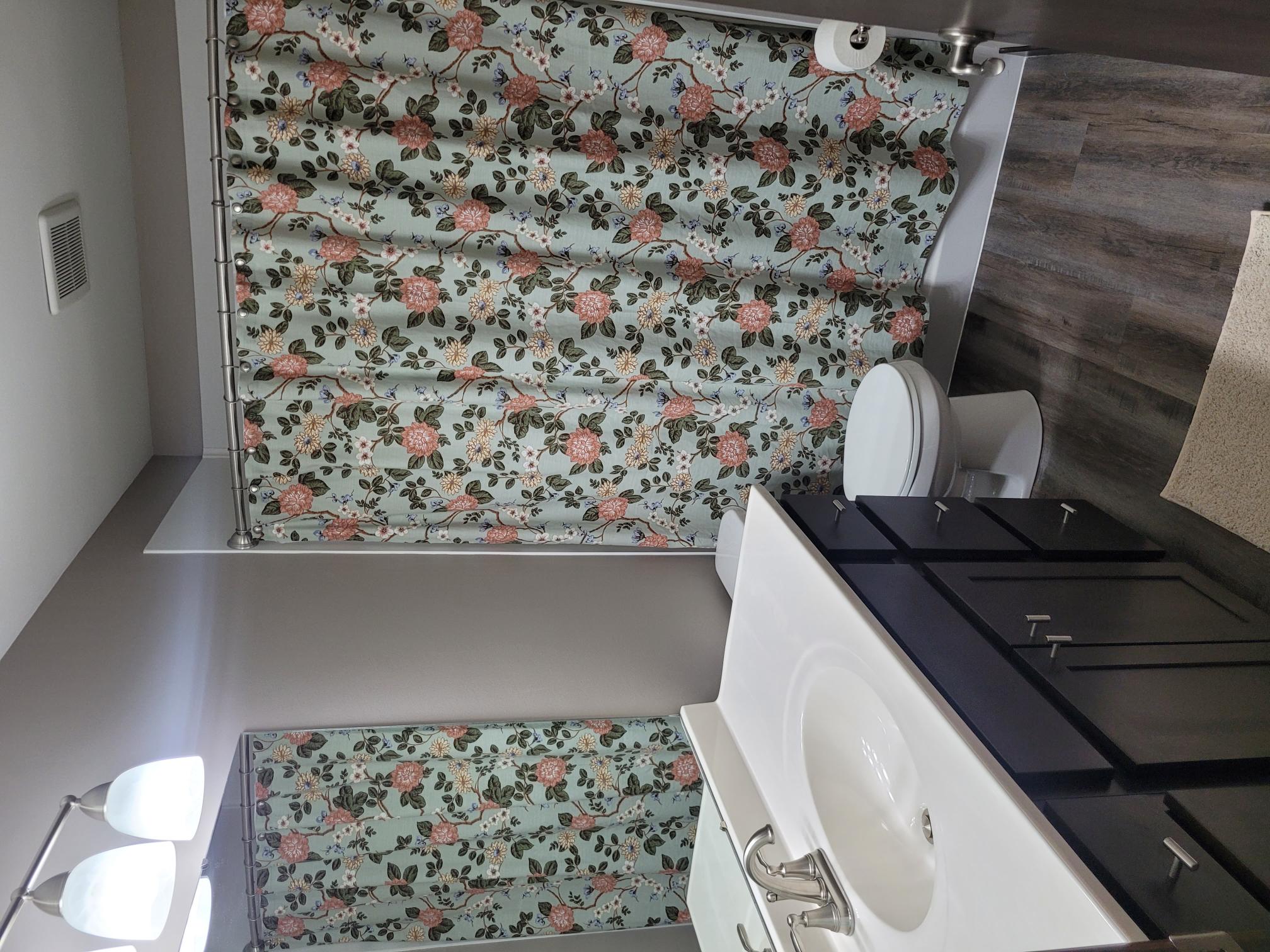 A bathroom with a floral shower curtain and matching bath mat.