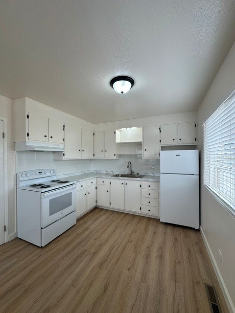 A white kitchen with wood floors and white appliances.