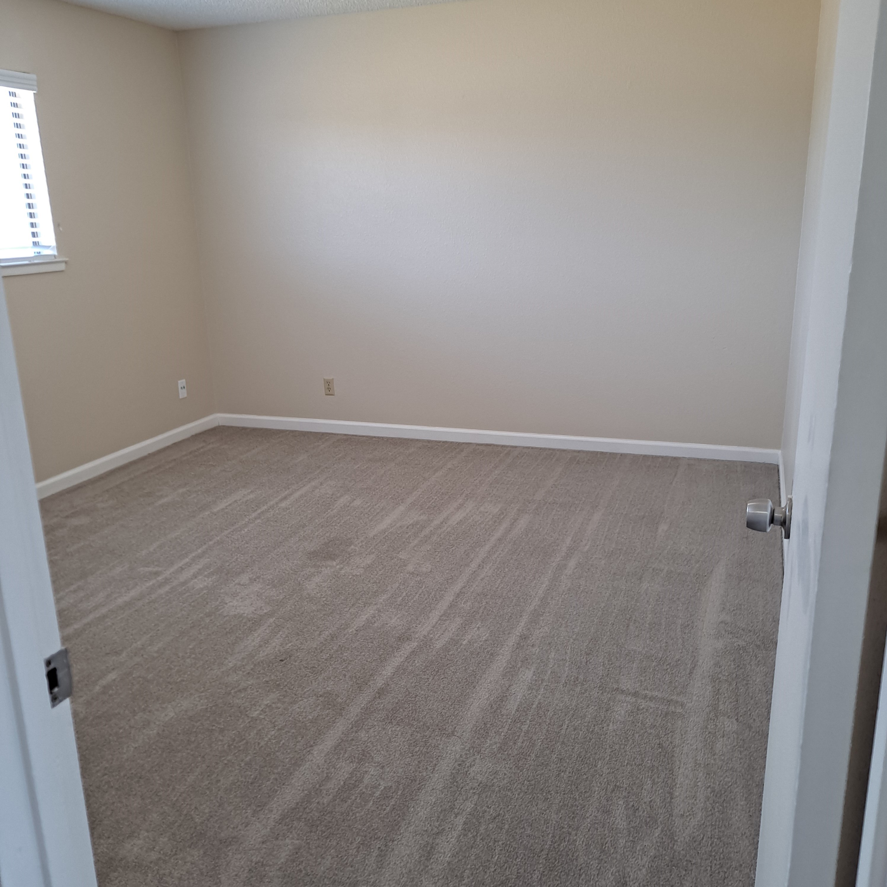 A room with a carpeted floor and a door on the right side.