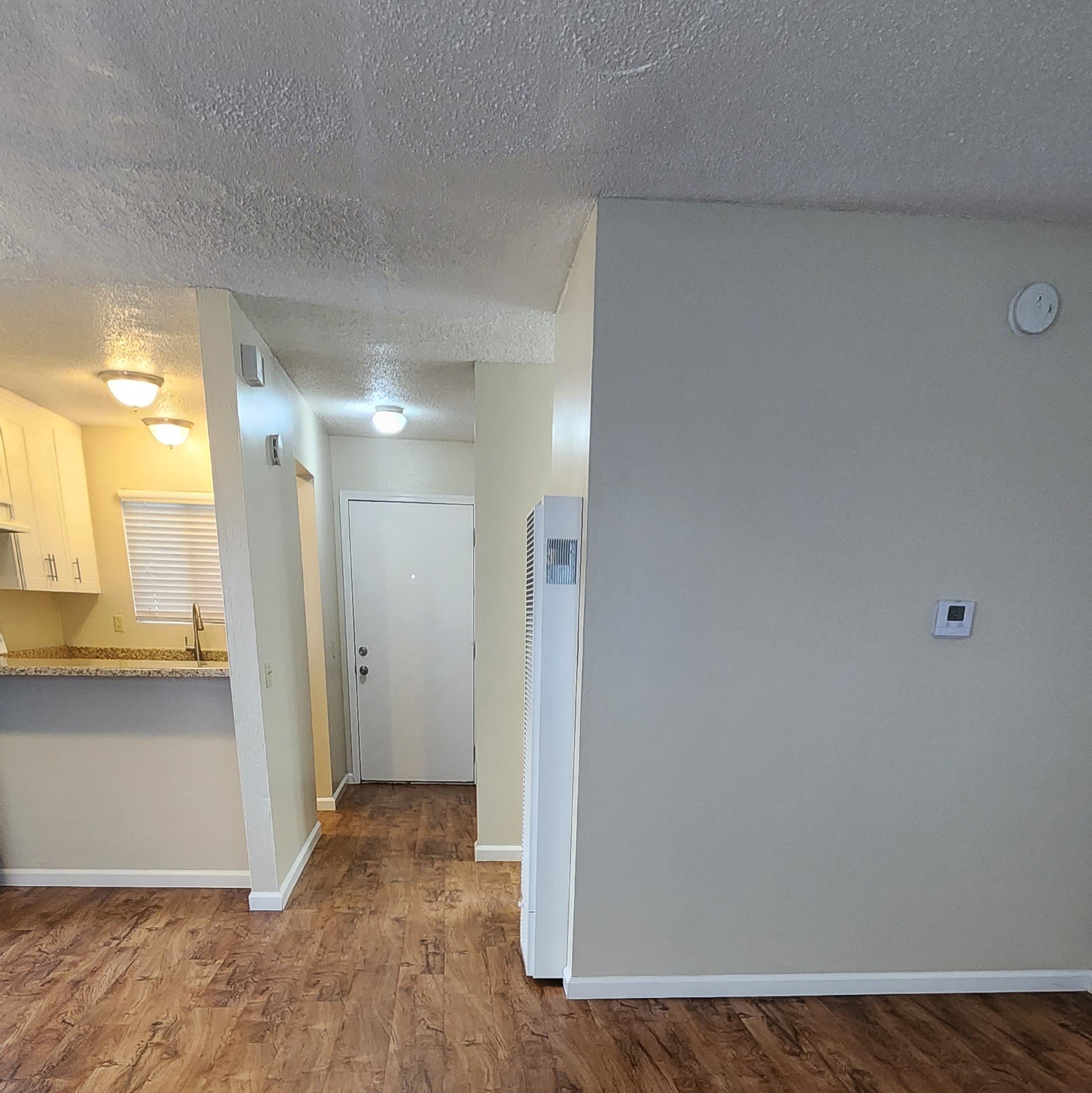 the living room and kitchen of an apartment with a hard wood floor and white walls