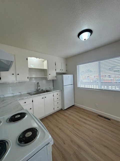 A kitchen with a white stove top oven and white cabinets.