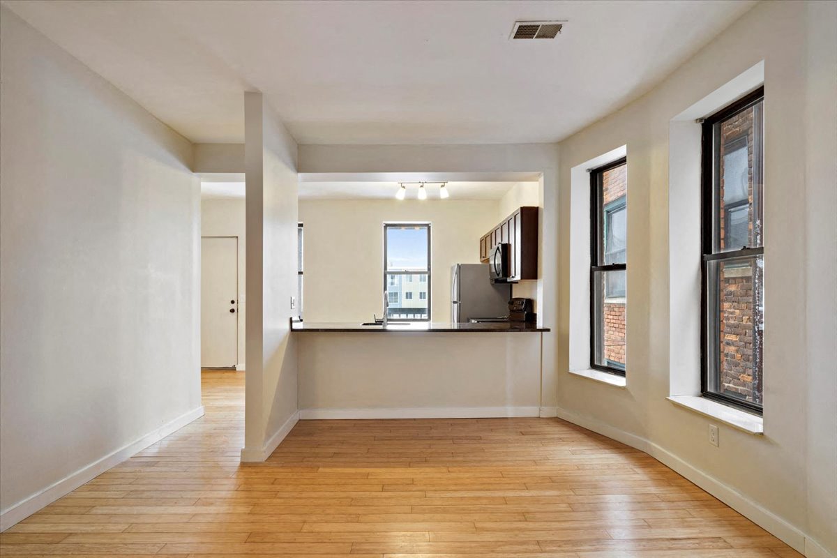 an empty living room with hardwood floors and a kitchen in the background