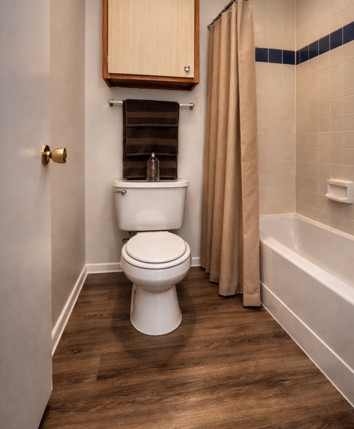 A white toilet in a small bathroom with a wooden cabinet above it.