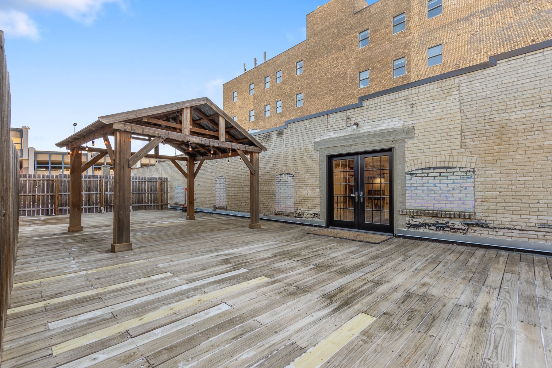 A wooden deck with a pavilion and a brick building in the background.