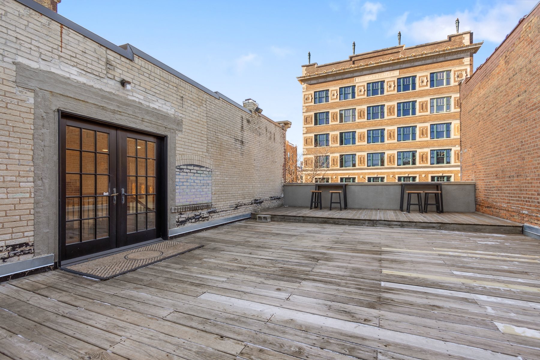 A wooden deck with a glass door and a brick building in the background.