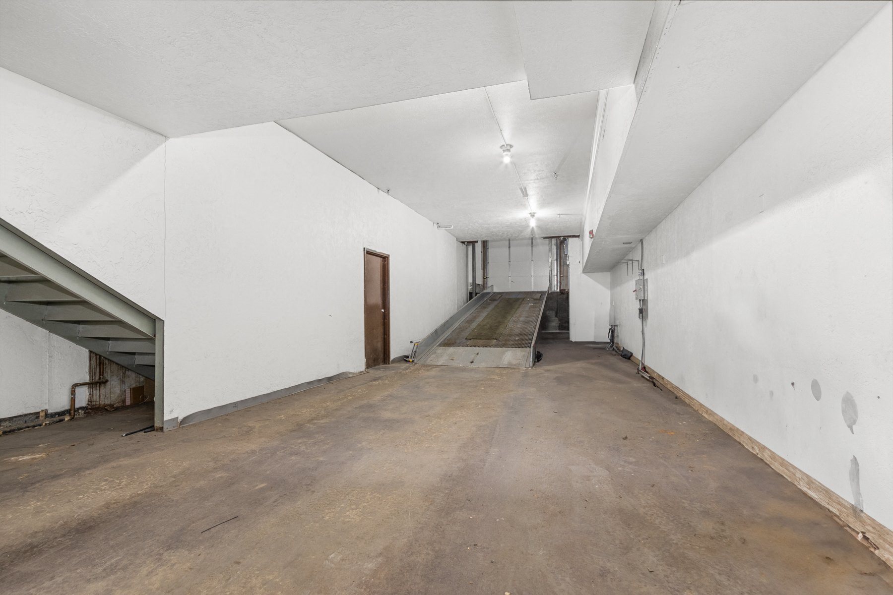 A large empty room with a staircase and a door.