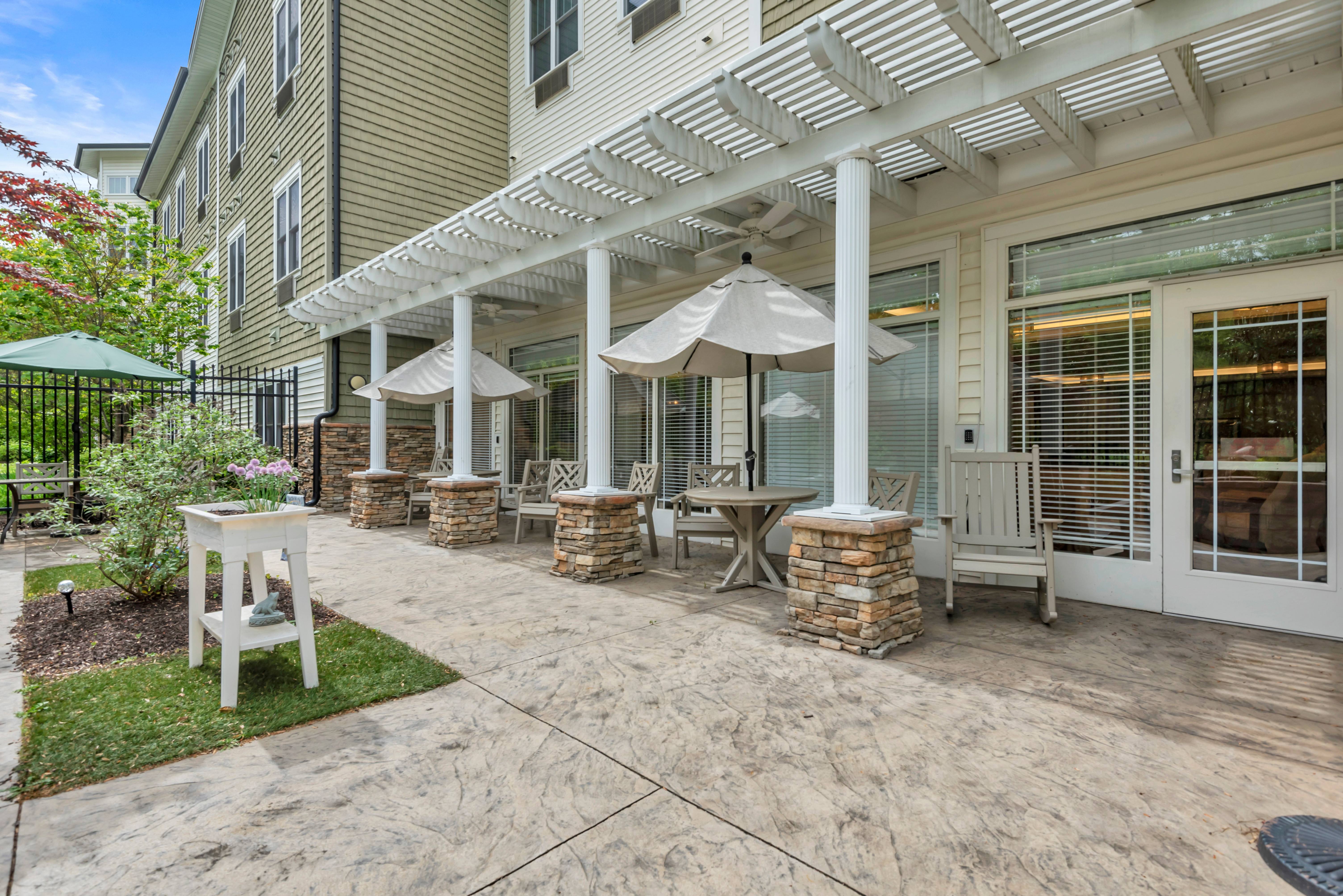 A patio with a table and chairs under a white pergola  of Spring Arbor of Severna Park